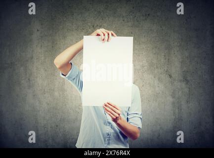 A young man holds a sheet of white paper in front of his face Stock Photo