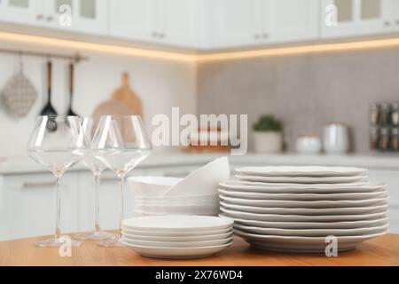 Clean plates, bowls and glasses on wooden table in kitchen Stock Photo
