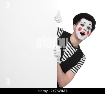 Funny mime artist peeking out of blank poster on white background Stock Photo