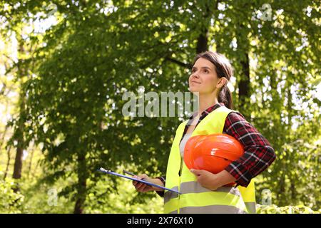 Forester with hard hat and clipboard examining plants in forest, space for text Stock Photo