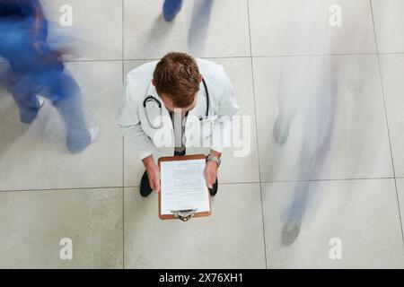 Above, doctor and busy hospital with clipboard, report or document for patient file. Man, high angle and notes for health insurance, medicine or drug Stock Photo