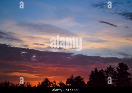 Morning glow illuminates the clouds on a beautiful colorful sky above the silhouettes of trees at dawn Stock Photo