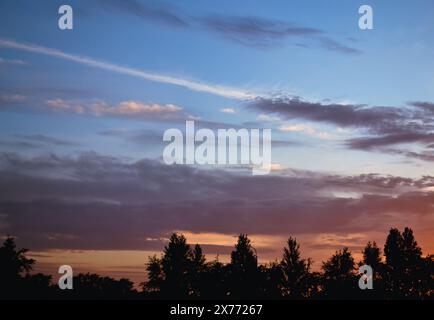 Morning glow illuminates the clouds on a beautiful colorful sky above the silhouettes of trees at dawn Stock Photo