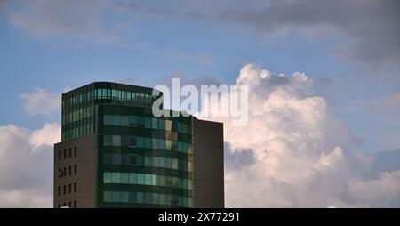 Skyscraper with a glass facade against the backdrop of a large white cloud in the evening sky Stock Photo