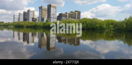 Construction of a residential complex on the banks of the river. Multi-storey buildings surrounded by trees are reflected in the river against the blu Stock Photo