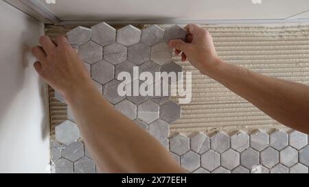 A tiler installs spacers between ceramic tiles. Gray tiles - mosaic in the kitchen. A tiler is gluing mosaic tiles to a kitchen backsplash. A man is Stock Photo