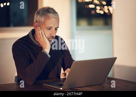 Male programmer, working and laptop in home at night for career, planning for coding or programming. Mature man, dark and house with computer for job Stock Photo