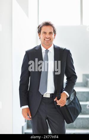 Happy, businessman and walking down stairs in portrait with laptop bag in office for travel. Smile, male person or entrepreneur with luggage for Stock Photo