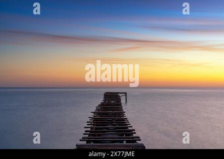 Peaceful sunrise seascape with an old wooden dock leading out into the calm ocean waters Stock Photo