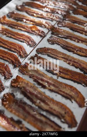 Freshly cooked crispy bacon strips cooling on a parchment-lined baking sheet Stock Photo