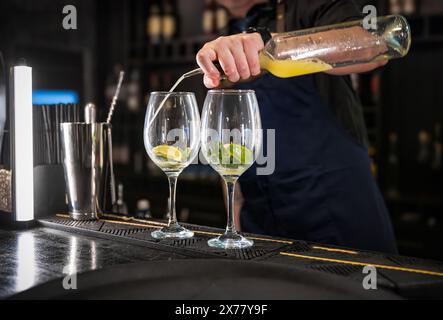 Close-up of a bartender skillfully pouring a mixed drink into two elegant glasses with lime Stock Photo