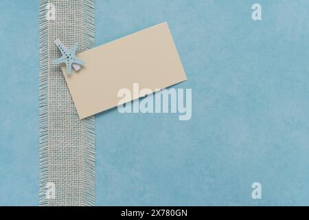 soft blue textured background with natural white burlap ribbon border and off white blank card held with blue starfish clip Stock Photo