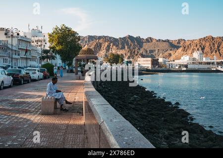 A man sits on a seat at the seawall in Sultan Qaboos Port, Muscat, Oman, at sunset Stock Photo