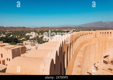 Curved defensive wall of Nizwa Fort overlooking the city's date palm oasis and Hajar Mountains under a clear blue sky in Oman Stock Photo
