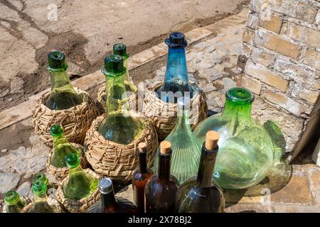 A variety of glass bottles, some in woven baskets, are displayed outside the store. Sunlight highlights their bright colors in Kashan, Iran. Stock Photo