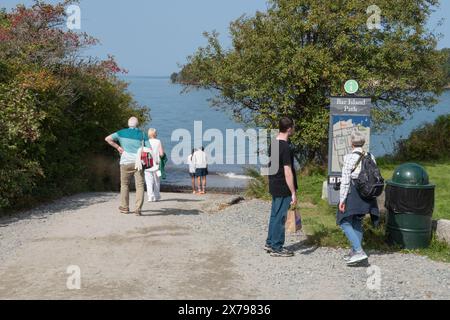 Tourists-visitors to Bar Harbor read the Bar Island Path map and gaze down Bridge St towards Frenchman's Bay at high tide. Mount Dessert Island, Maine Stock Photo