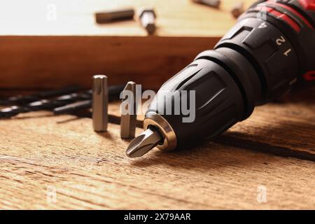 Electric screwdriver with bits and drills on wooden table, closeup Stock Photo