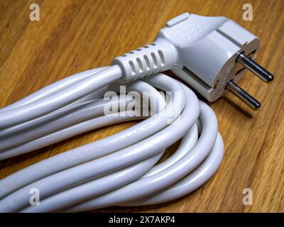 Nizhyn, Ukraine, September 25, 2021. Coiled white cable with a two-prong plug, set on a wooden table, symbolizing electricity in domestic settings. Il Stock Photo