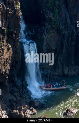 A speed boat loaded with tourists sits adjacent to a waterfall flowing into the Iguazu River at Iguazu Falls in Brazil. Stock Photo