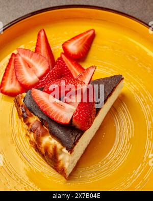 Strawberry garnished cheesecake slice on yellow plate Stock Photo