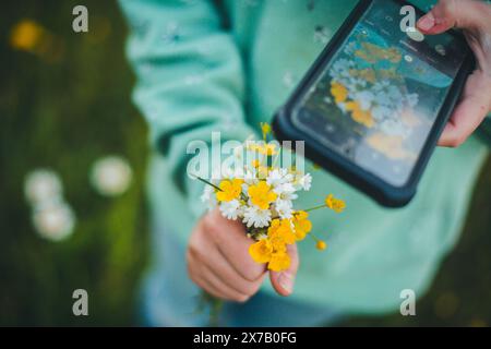 Girl taking pictures of a nosegay of picked flowers, using her mobile phone Stock Photo
