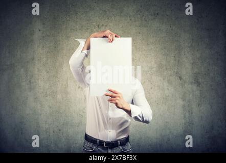 young man holds a sheet of white paper in front of his face, hiding his identity Stock Photo
