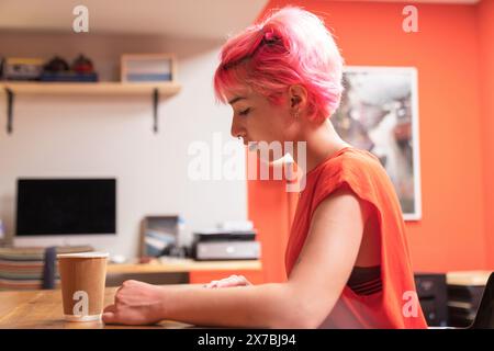young woman working while drinking coffee in the office. Generation Z woman with pink hair works in the office or at home Stock Photo