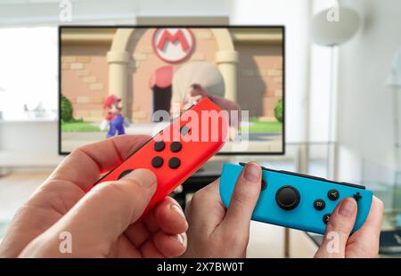 Close up of hands og people playing Mario vs. Donkey Kong on a new Nintendo Switch console in handheld mode. Popular mobile console. Copenhagen, Denma Stock Photo