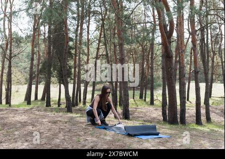 A young woman is preparing to practice yoga in the forest. A girl lays out a yoga mat. Stock Photo