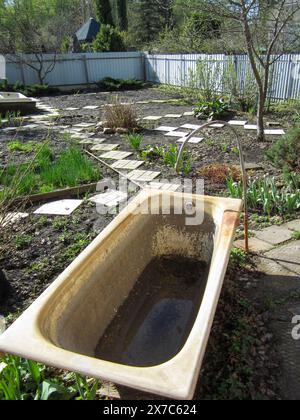 Cottage yard with old cast iron tub for collecting water and watering plants in drought. Vegetable garden. Stock Photo