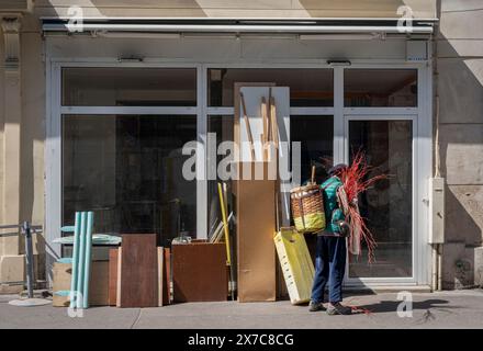 Paris, France - 05 11 2024: View of an old gleaner woman carrying a hood on his back in front of bulky items in a closed store Stock Photo