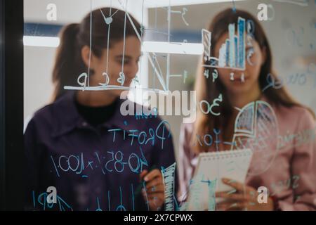 Corporate strategy and teamwork in action: Two business professionals analyze data on a glass board Stock Photo