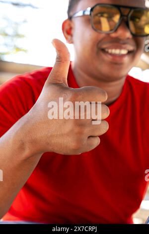Vertical portrait smiling young black man pointing thumb up on blur background Stock Photo