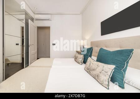 Bedroom with two single beds joined by a fabric-upholstered headboard, lamps with two shades and a large wardrobe with sliding mirror doors Stock Photo