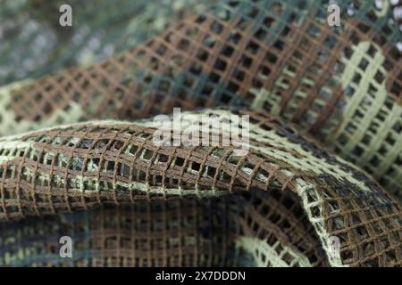 A piece of camouflage fabric with a green and brown pattern. The fabric is made of a mesh material and has a rough texture Stock Photo