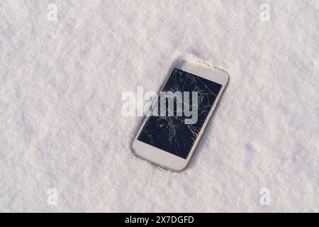 Broken mobile phone with cracked display over natural snow background,outdoor,natural light Stock Photo