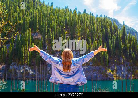 Woman looks at a sunken forest in the mountain lake Kaindy in Kazakhstan. Panoramic view of the unique lake. Nature reserve. Stock Photo