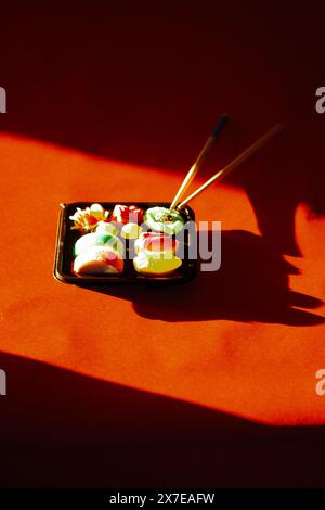 Jelly candies Sushi set in a black box on red background Contrast dark shadows. Wooden sushi sticks chopsticks. Asian Japanese. Chinese sweet food. Stock Photo