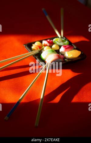 Jelly candies Sushi set in a black box on red background Contrast dark shadows. Wooden sushi sticks chopsticks. Asian Japanese. Chinese sweet food. Stock Photo