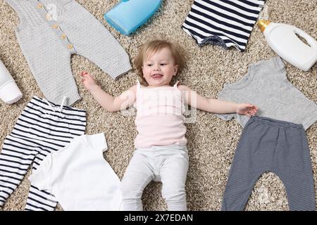 Little girl among baby clothes and detergents on carpet, top view Stock Photo