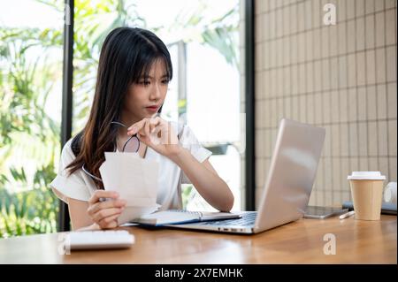A professional, beautiful millennial Asian businesswoman or female accountant is checking bills and receipts, working on business financial data on he Stock Photo