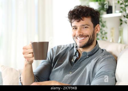 Happy man drinking coffee sitting on a couch at home looking at camera Stock Photo