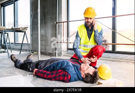 Colleague giving first aid to unconscious worker after accident, calling ambulance. Concept of occupational safety and health in workplace. Stock Photo