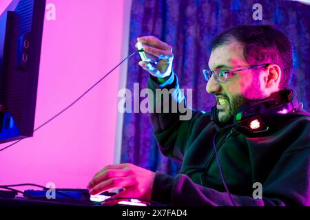 Streamer Angry computer gamer man yells and breaks keyboard after being defeated in online video game. Stock Photo