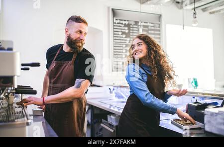 Two young baristas working in coffee shop, standing by counter. Teamwork. Stock Photo