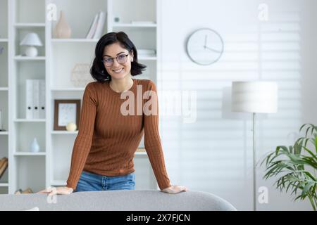 Smiling woman wearing glasses and casual clothes standing confidently in a bright home office environment. Stock Photo