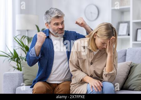 Middle-aged couple having a heated argument in their living room. The man is visibly angry while the woman looks distressed and upset. Stock Photo