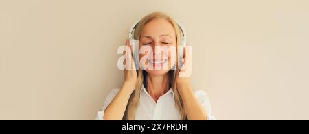 Portrait of happy relaxed middle aged woman listening to music in wireless headphones on white background Stock Photo