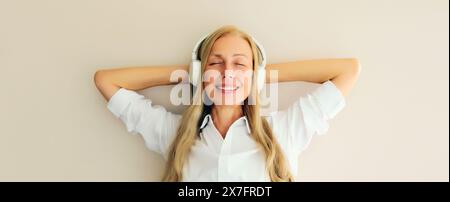 Portrait of happy relaxed middle aged woman listening to music in wireless headphones on white background Stock Photo