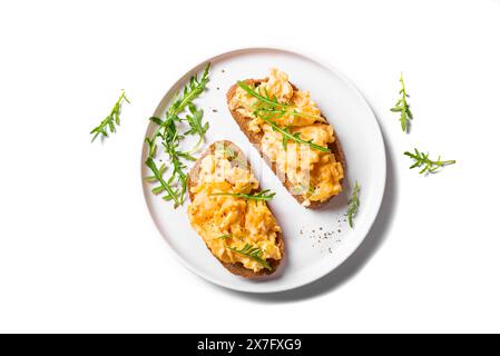 Scrambled Eggs Sandwiches on white plate isolated on white background, healthy keto breakfast. Whole grain toasts with scramble eggs and organic arugu Stock Photo